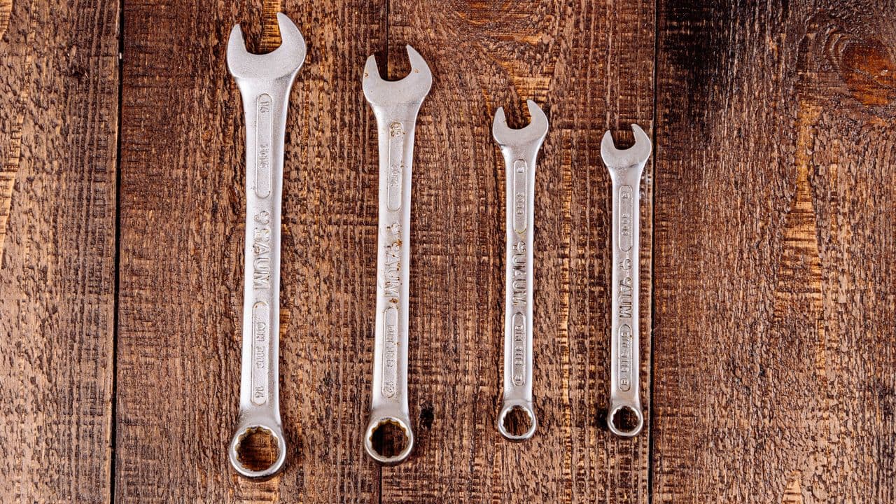 Four metal wrenches laid out on a wooden workbench surface