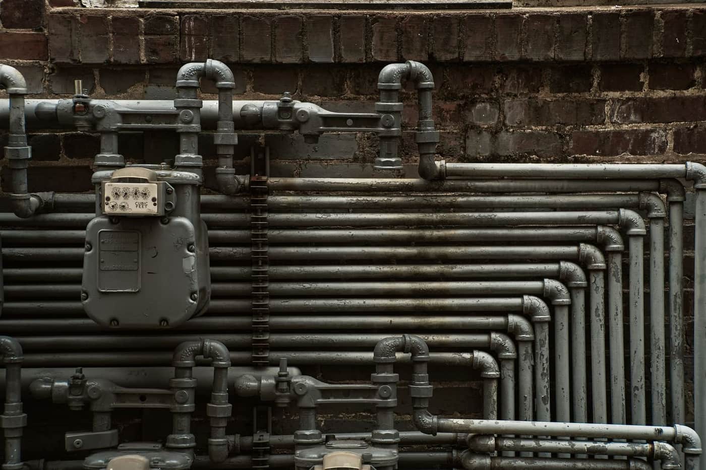 Industrial steel pipes and a gas meter mounted on a commercial brick building exterior