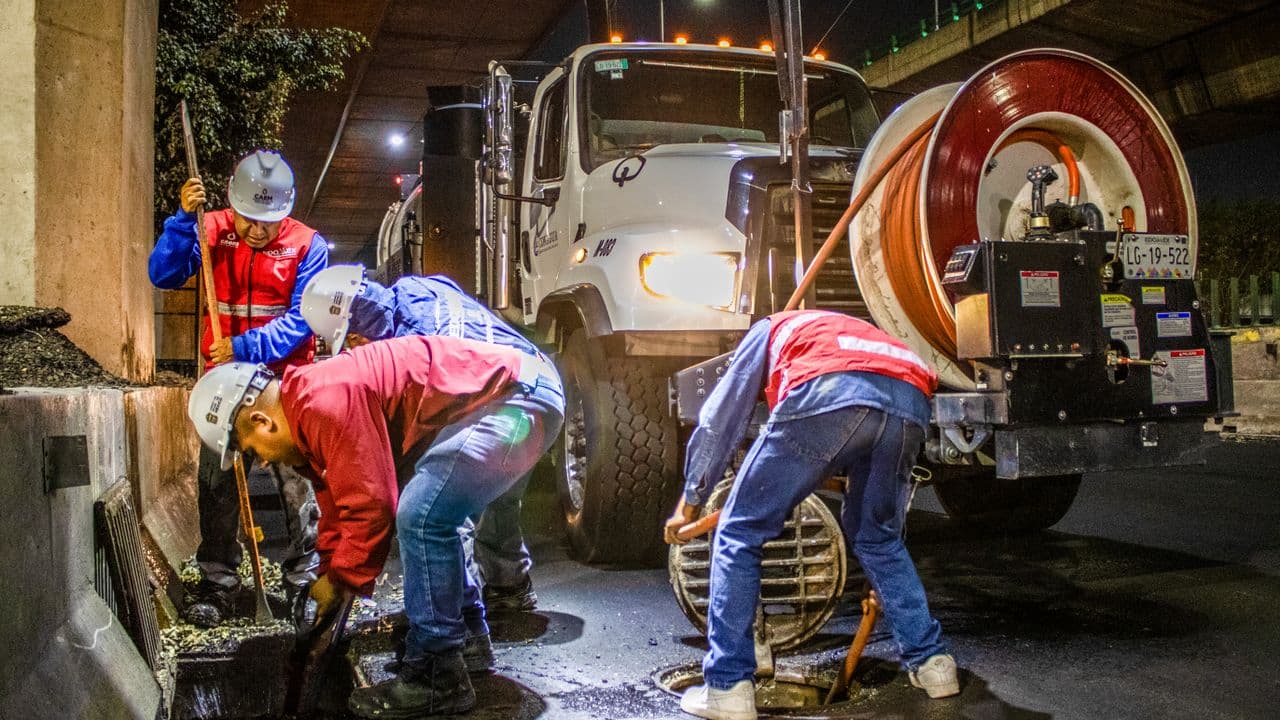 Crew cleaning a drainage line at night with a sewer machine under a bridge
